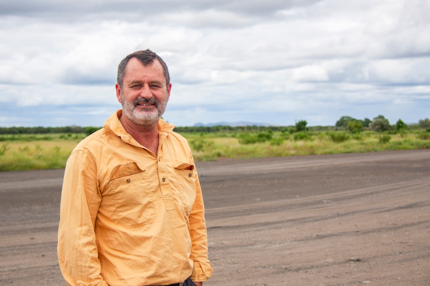 man stands under cloudy sky and smiles.