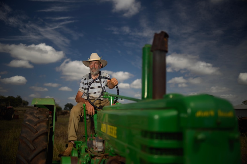 Mervyn Polzin sits on the back of an old John Deere tractor, blue sky with a few clouds.