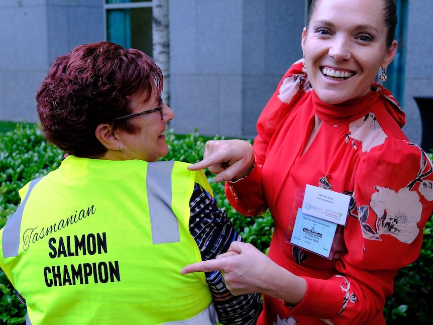 A woman with short maroon coloured hair wears a bright green vest with "salmon champion" emblazoned on the back
