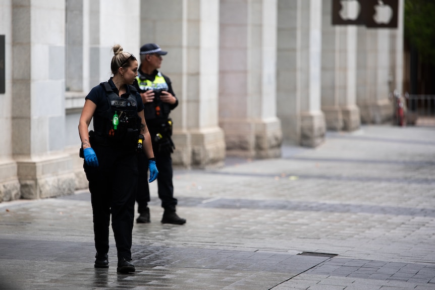 A detective looks at the ground as she walks down a pedestrian mall.