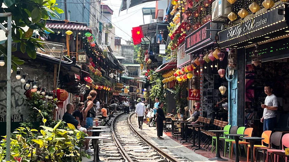 Hanoi, Vietnam - 24 December 2024: Hanoi's famous Train Street, a train approaches, passing close to vibrant cafes with colorful lanterns. Locals and tourists stand aside, capturing the unique vibe.