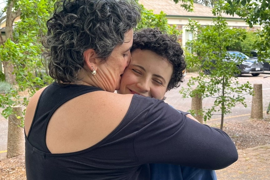 As woman with short curly hair hugs her adult child tight.