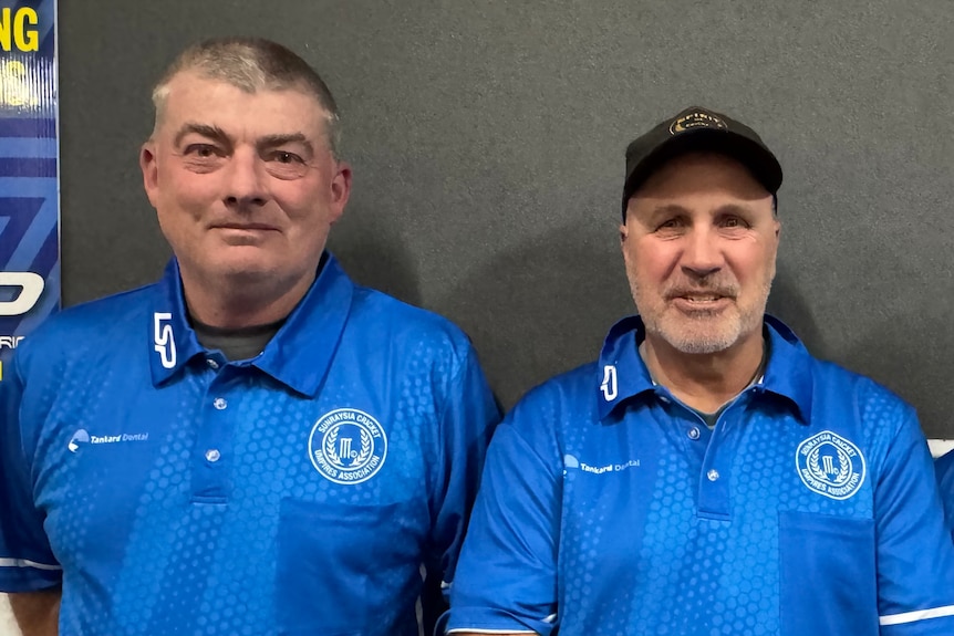 Two men sit side-by-side dressed in blue t-shirts.
