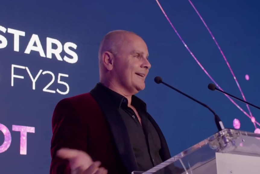 A man stands at a podium speaking into a microphone.