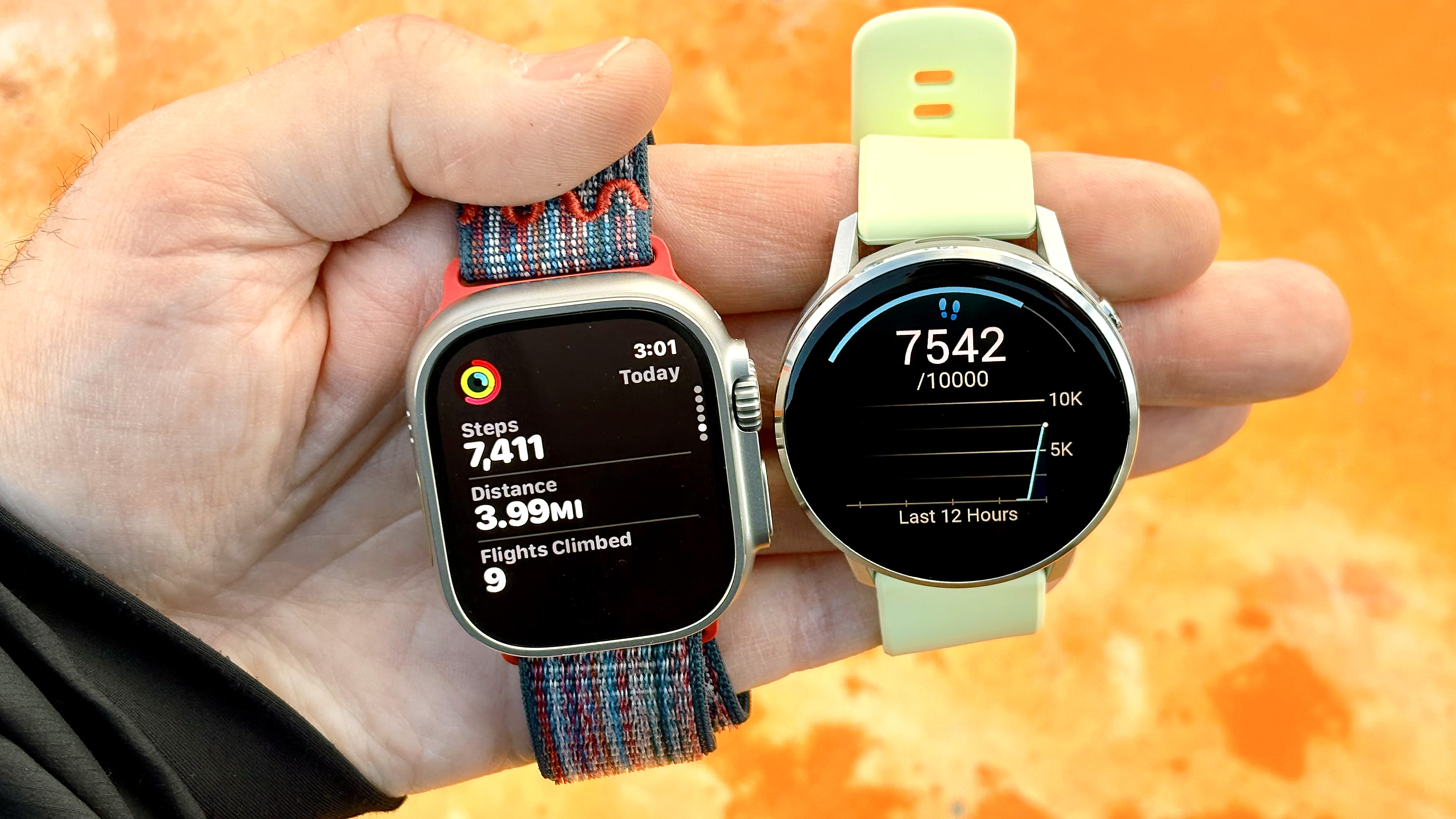 Close-up of the Garmin Venu 4 and Apple Watch Ultra 3 against a weathered orange background