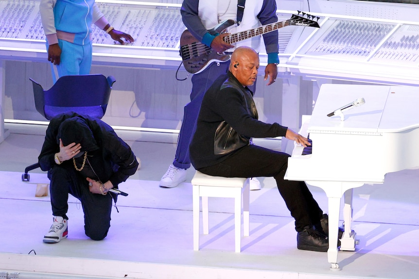 One artist takes a knee, next to another artist playing the piano