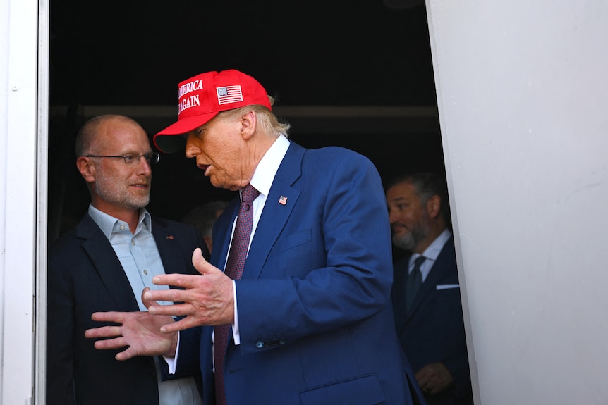 Donald Trump wearing a red MAGA cap standing next to Brendan Carr in a doorway.