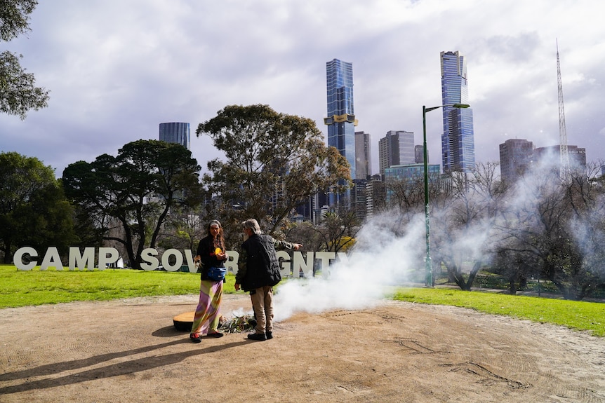 Smoke and two people at Camp Sovereignty, with the city skyline in the background