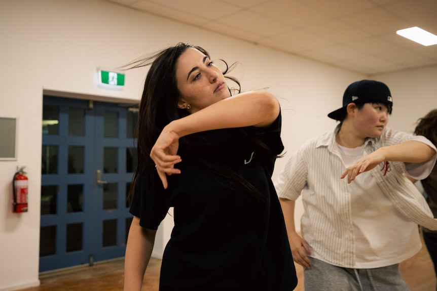 A woman with dark hair and dark tshirt dancing in a room with others