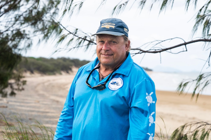 A man standing at a beach wearing a blue volunteer shirt
