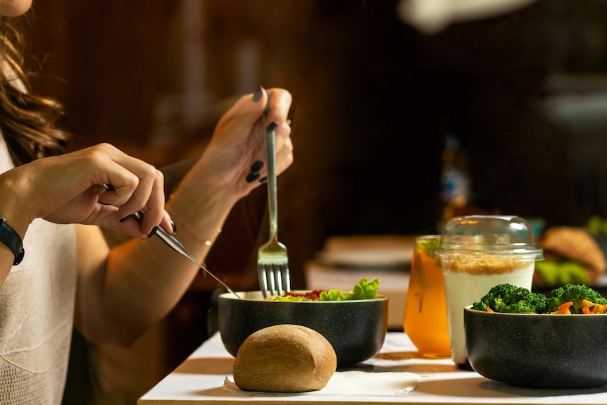 Woman eats salad with cutlery at a table