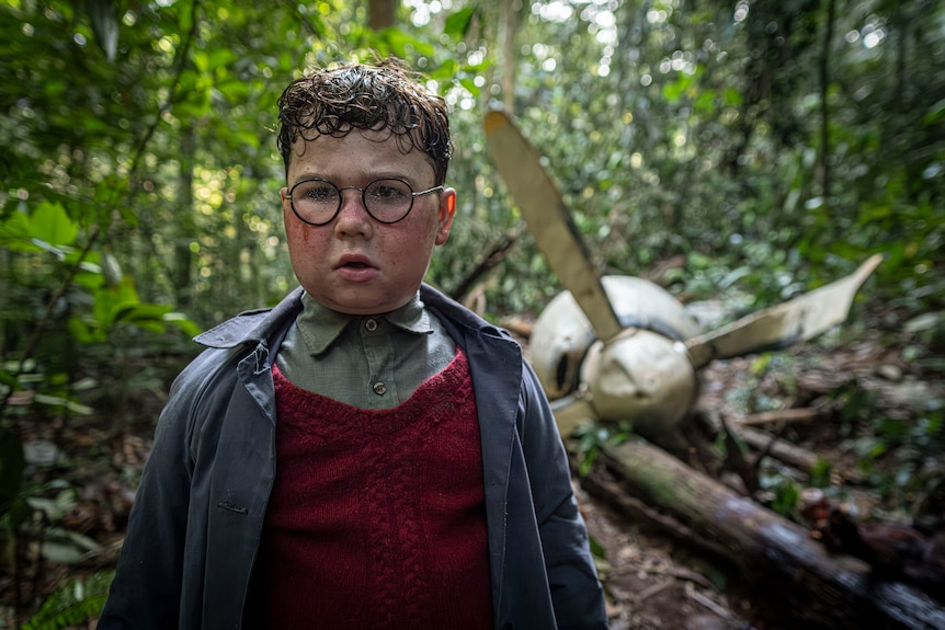 A TV still of David McKenna, 12, with glasses, looking shocked in a forest. Behind him is the propeller of a crashed plane.