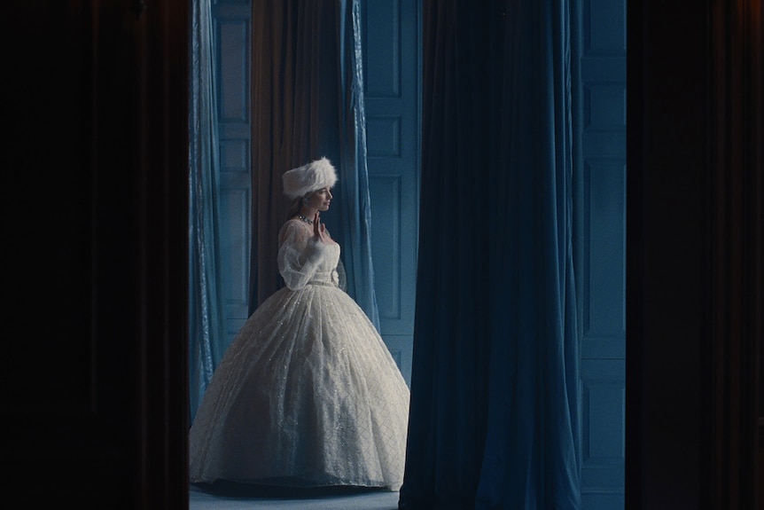 A woman in a puffy white wedding dress walks through a forest.