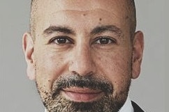 A headshot of a man with a beard, who is wearing a suit and tie. 
