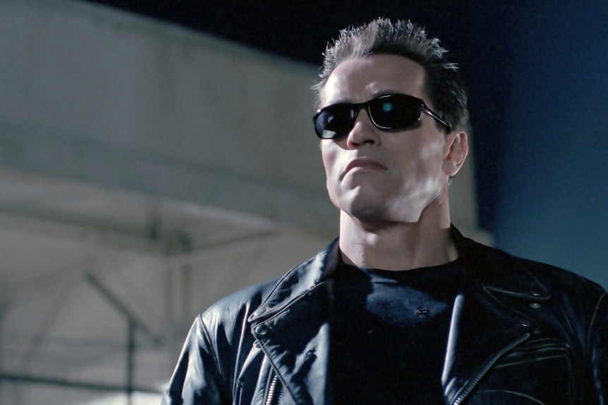 A man in sunglasses and a leather jacket outside a building at night.