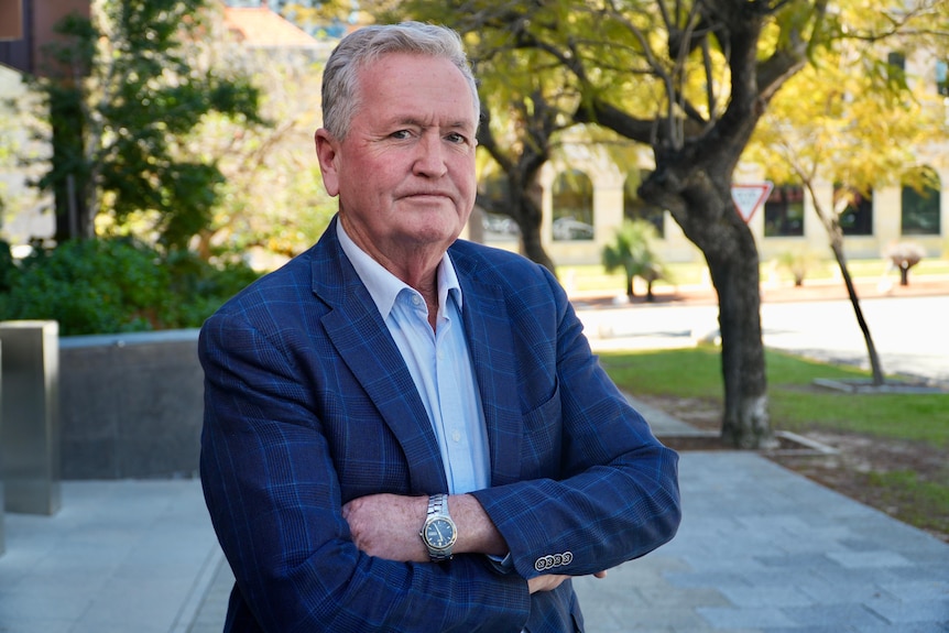 Shane Love wears a blue suit and smiles with his arms folded