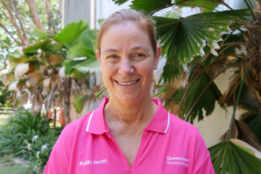 A woman smiling and standing in front of a garden.