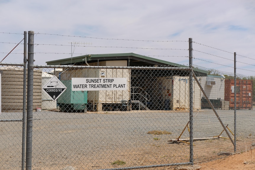 A high mesh gate outside the water treatment plant with shipping containers seen under a shed