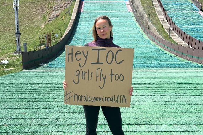 Annika Malacinski holds a sign at the base of a ski jump