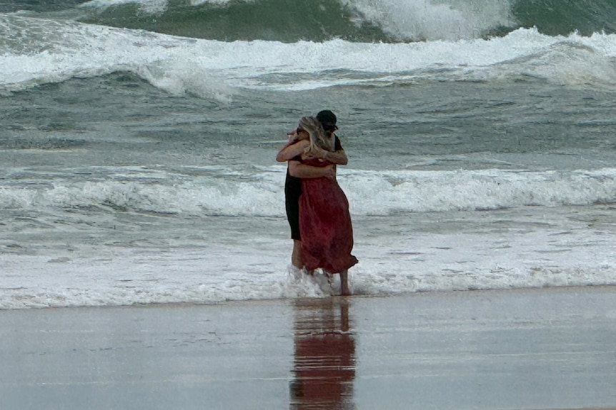 A couple embrace at the ocean's edge.