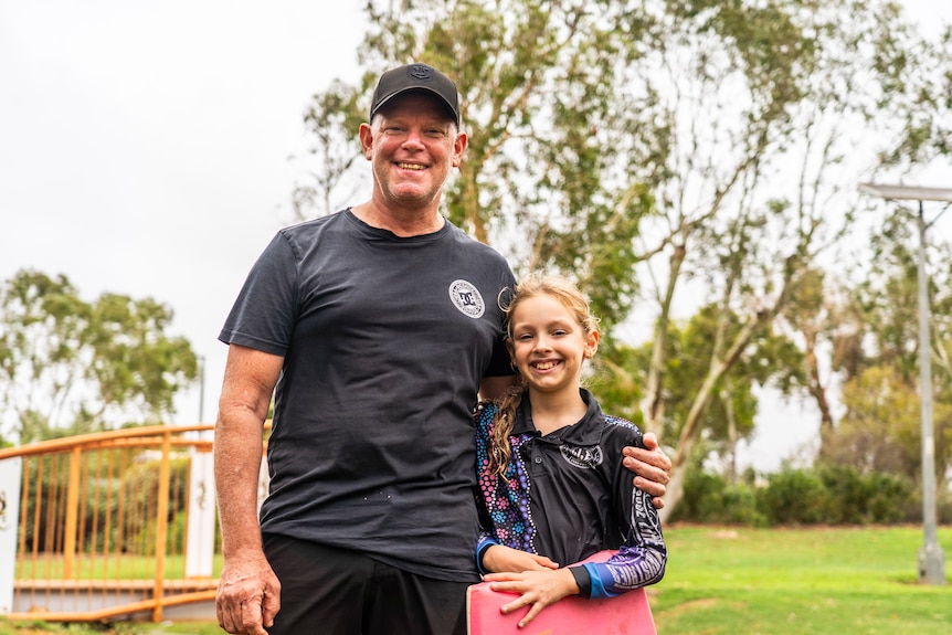 A man in a dark shirt with a girl with a boogey board
