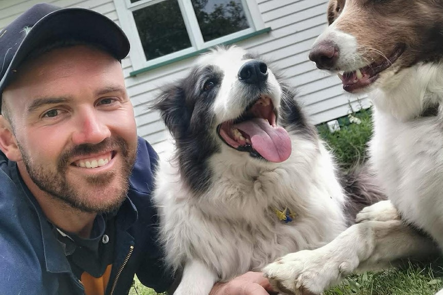A young man wearing a cap on the grass next to a smiling border collie