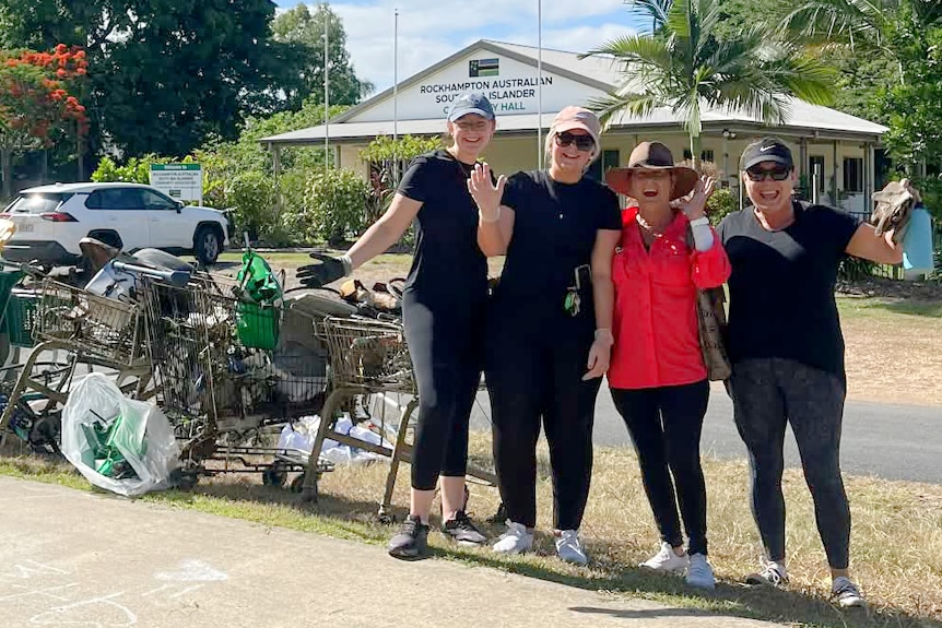 Four women stand next to trolleys and rubbish
