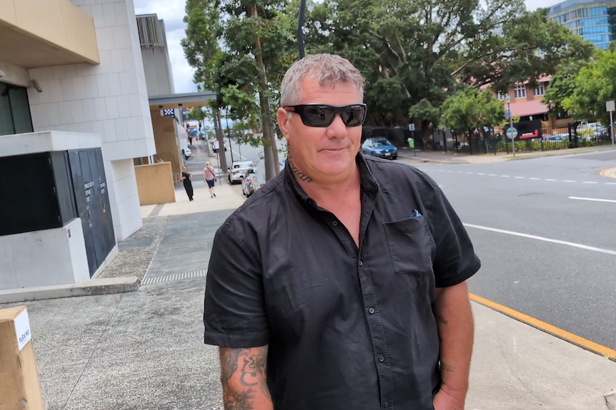 A man in a blue shirt and dark sunglasses on the street