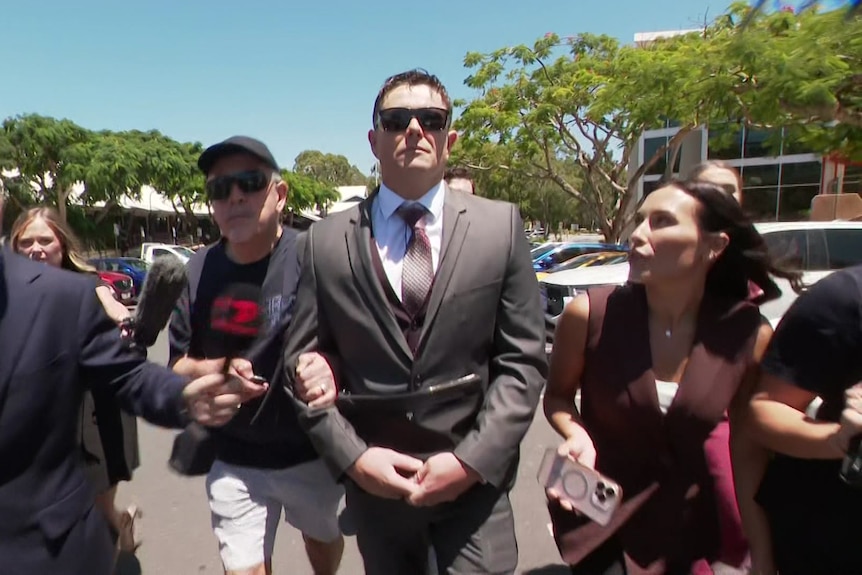 A man in a suit walking while reporters ask him questions