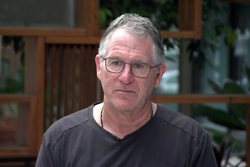 Criminologist Dr Vincent Hurley wearing glasses and a t-shirt stands outdoors talking to the media