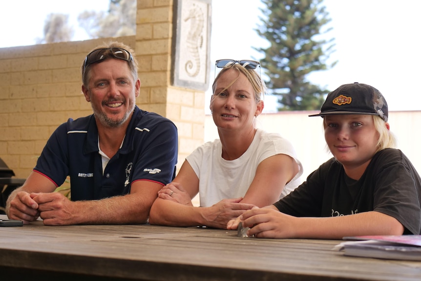 A man, woman and young boy sit at a table and smile at the camera.