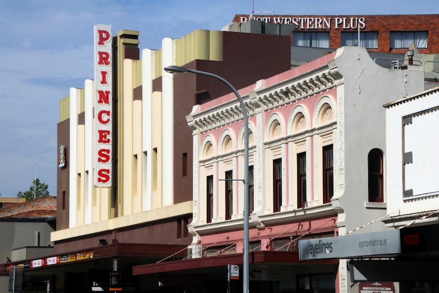 A side profile of a baby pink building next to a building with a red neon sign that reads PRINCESS.