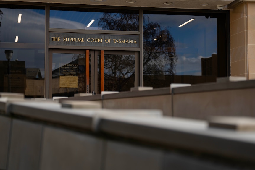 A sign at the front of a glass and brick building which reads 'Supreme Court'.