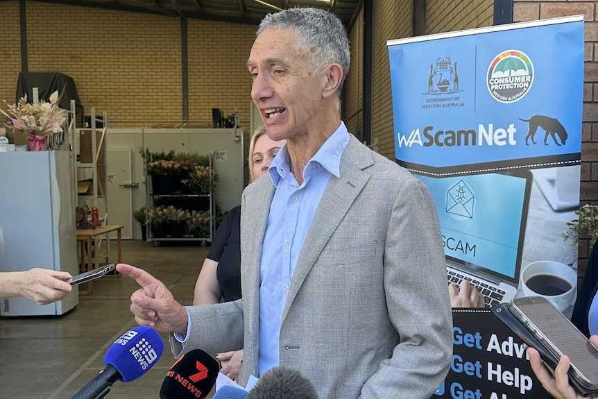 Tony Buti stands in front of microphones speaking and pointing with his finger. 