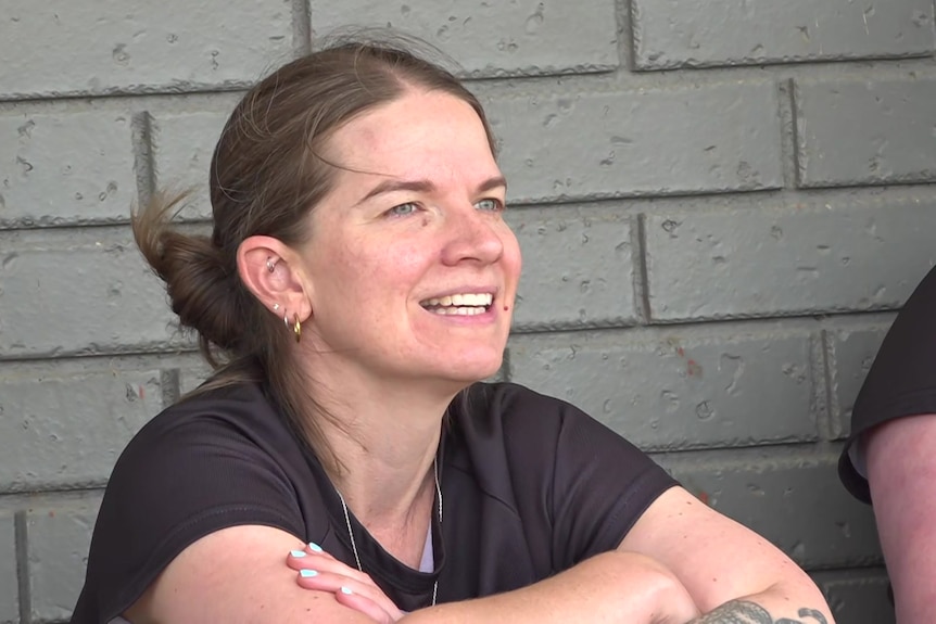 a woman in training gear looks out past the camera view wit her arms crossed   