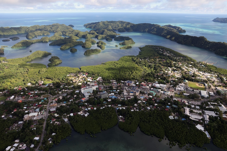 aerial shot of island city of houses and roads surrounded by jungle and small rock islands