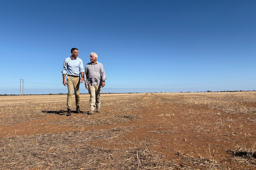 Peter Malinauskas and a farmer walk across a dry field.