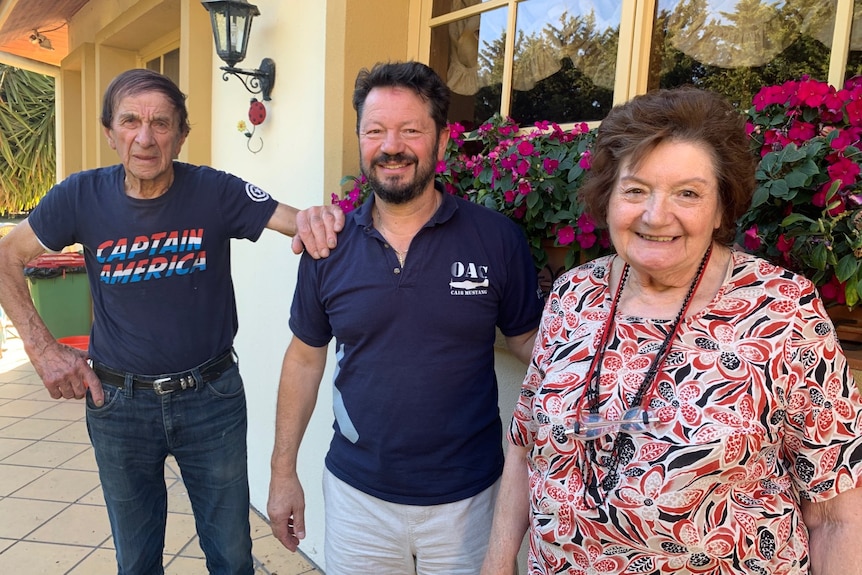 An elderly man wearing a Captain America T-shirt with a younger man and a woman wearing a floral top.