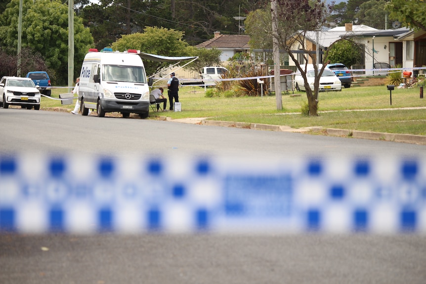 Police tape in the foreground, a police car near a home in the distance.