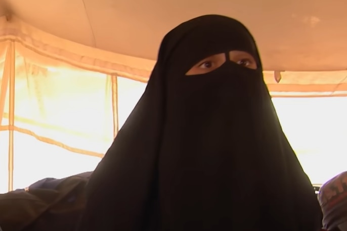 A woman with brown eyes wearing a burqa sits speaking in a tent.