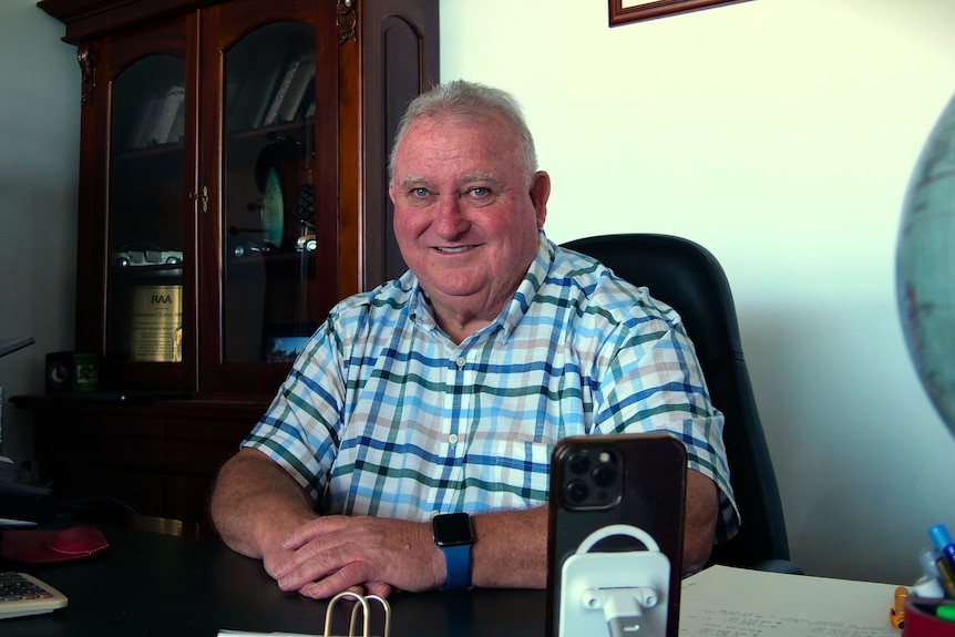 A man sits at a desk with crossed hands. 