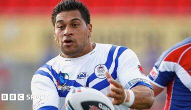 Matt Utai throws a rugby ball and is wearing a white and blue t-shirt