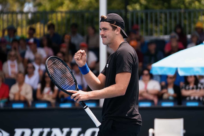 A man on a tennis court punches the air in excitement