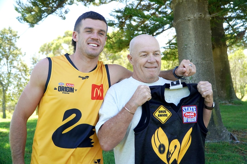 Jake and Chris Waterman standing side by side, Jake wearing a WA guernsey and Chris holding his up. 