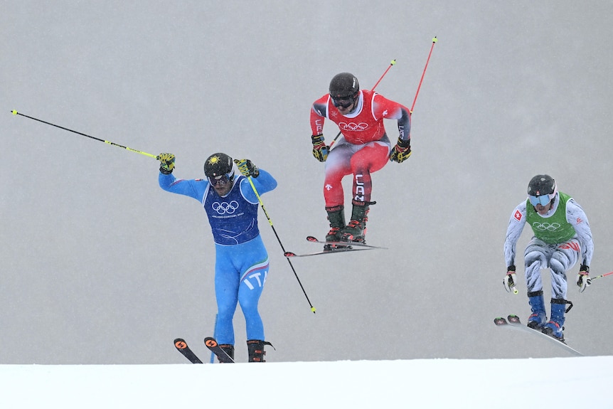 Three skiers jump in heavy snow.