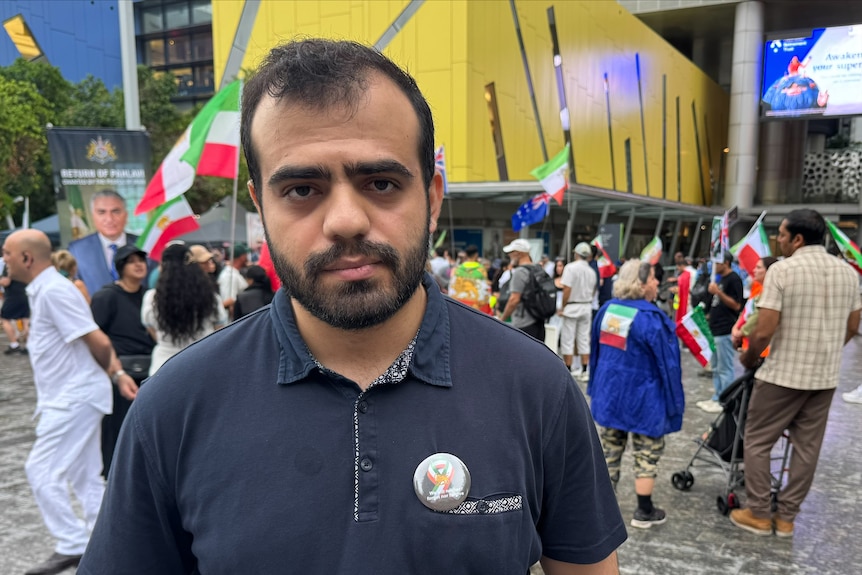 A man stares at the camera while others march in the background holding flags and signs