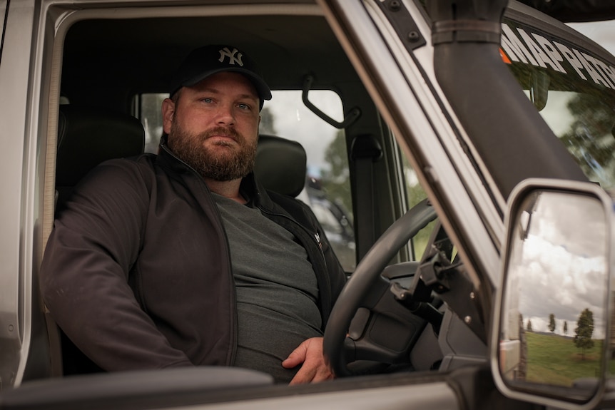 A man sits in the driver's seat of a 4WD, one arm resting on open window