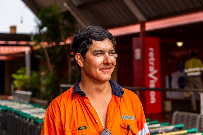 A young man with short black hair wearing a high-vis shirt smiles.