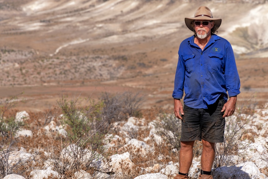 Calum Caruth stands in front of the Pilawarra land system — a sparse rocky landscape with some tough grasses.