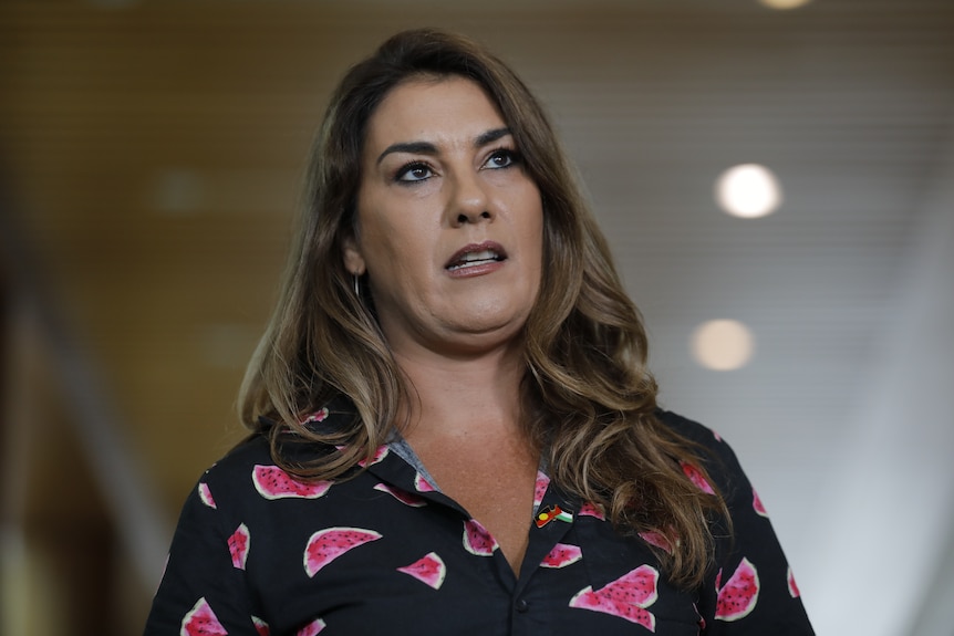 A woman with long brown hair speaking while looking off camera.